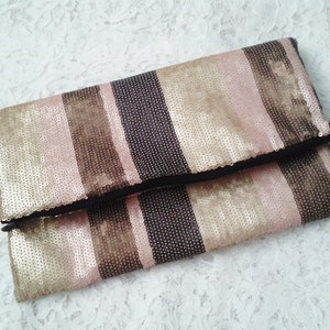 May include: A gold, brown, and pink striped clutch purse with a zipper closure. The purse is made of sequins.