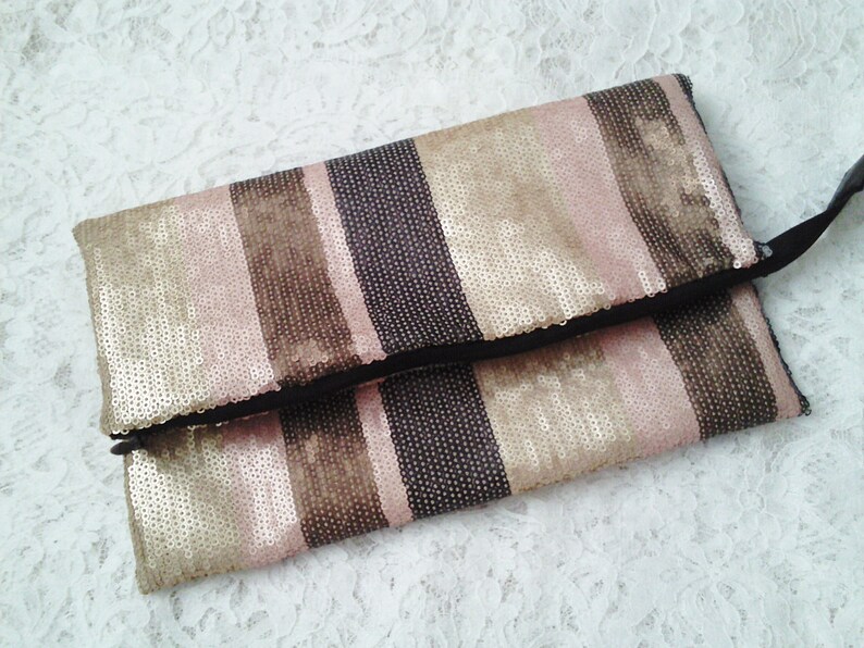 May include: A gold, brown, and pink striped clutch purse with a zipper closure. The purse is made of sequins.