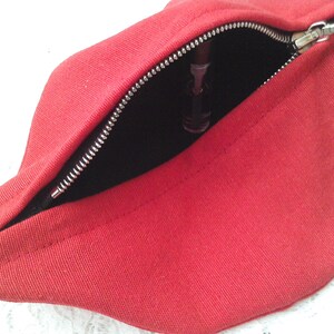 May include: Red fabric pouch with a zipper opening. The pouch is open and a black object is visible inside.