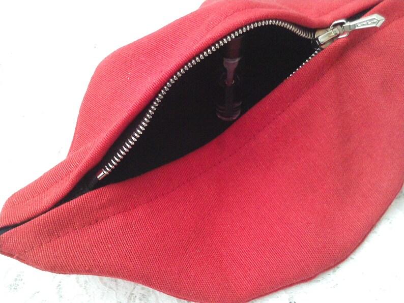 May include: Red fabric pouch with a zipper opening. The pouch is open and a black object is visible inside.