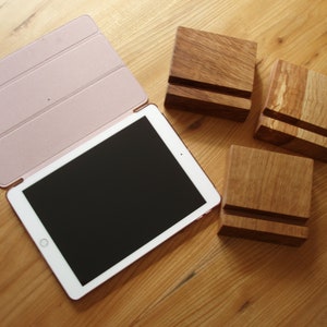 May include: Three wooden tablet stands in various shades of brown. The stands are made of solid wood and have a simple, minimalist design. A pink tablet case is also visible in the image.