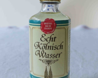 May include: A small glass bottle of cologne with a gold cap. The label is white with green and blue accents and reads "Echt Kölnisch Wasser Eau de Cologne Dom-Apotheke".