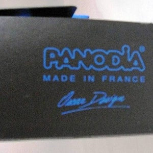 K&ouml;nnte beinhalten: Eine schwarze Box mit einem blauen Logo, auf dem "PANODA" und "MADE IN FRANCE" steht. Die Box tr&auml;gt au&szlig;erdem eine blaue Unterschrift mit dem Namen "Anne Degreve".