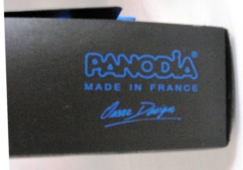 K&ouml;nnte beinhalten: Eine schwarze Box mit einem blauen Logo, auf dem "PANODA" und "MADE IN FRANCE" steht. Die Box tr&auml;gt au&szlig;erdem eine blaue Unterschrift mit dem Namen "Anne Degreve".