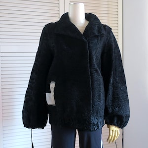 May include: A black textured jacket with a rounded collar and long sleeves. The jacket has a button closure and a slightly puffed sleeve design. The jacket is displayed on a mannequin. The jacket has a textured pattern.