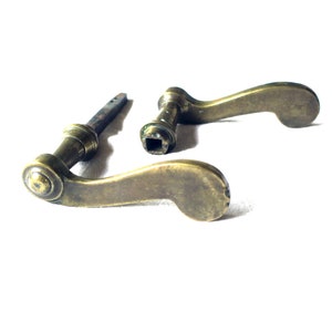 May include: Two antique brass door handles with a curved design. The handles are in a worn condition, showing signs of age and use.
