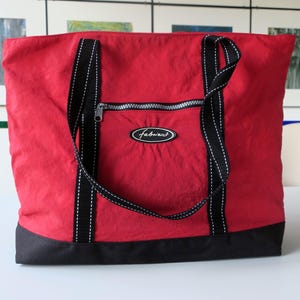 Könnte beinhalten: Eine rote Tragetasche mit schwarzen Akzenten. Die Tasche hat schwarze Träger mit weißen Nähten, einen schwarzen Boden und eine Reißverschlusstasche. Der Markenname "Fabriani" ist auf der Vorderseite zu sehen.