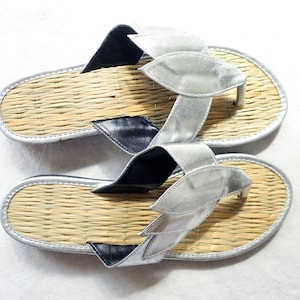 May include: A pair of silver and black sandals with woven straw soles. The sandals have a unique design with silver leaf-shaped straps.