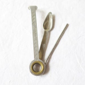 May include: A vintage silver and brass pipe tool, featuring a tamper, reamer, and pick. The tool has a rectangular handle with decorative etching and a circular brass ring. The spoon-shaped reamer and pick are made of silver metal.