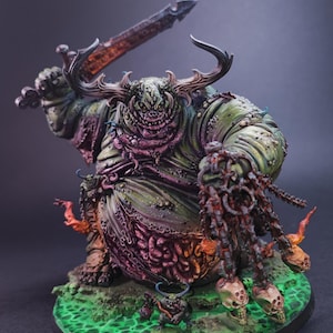 Puede incluir: Una figura miniatura de fantasía grande y corpulenta con piel verde y morada, cuernos y una amplia sonrisa. Sostiene una espada oscura en alto y una cadena con calaveras en la otra mano. Una criatura más pequeña está a sus pies sobre una base verde.