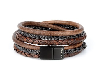 Puede incluir: Un brazalete de cuero multicapa con un cierre de metal negro. El brazalete presenta una correa de cuero trenzada y una correa de cuero lisa. El cierre tiene la palabra "INIVI" grabada.