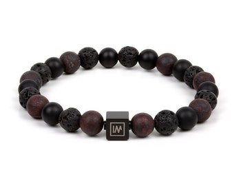 May include: A black beaded bracelet with red and black lava rock beads. The bracelet has a black metal square charm with the letter "W" engraved on it.