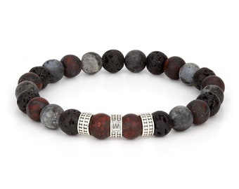 Op de afbeelding: Een kralenarmband met een mix van donkergrijze, rode en zwarte lavastenen kralen. De armband heeft een centraal gedeelte met rode kralen en zilverkleurige metalen accenten. De kralen zijn aan elkaar geregen, waardoor een cirkelvorm ontstaat.