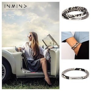 May include: Two leather bracelets with a silver clasp. The bracelets are made of braided leather in black and grey. The bracelets are shown on a model's wrist and on a white background.