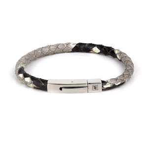 May include: A grey and black braided leather bracelet with a silver clasp. The clasp has a small metal logo with the letter "W" on it.