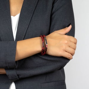 Puede incluir: Un brazalete de cuero rojo y negro con un cierre plateado. El brazalete se lleva en la mu&ntilde;eca.