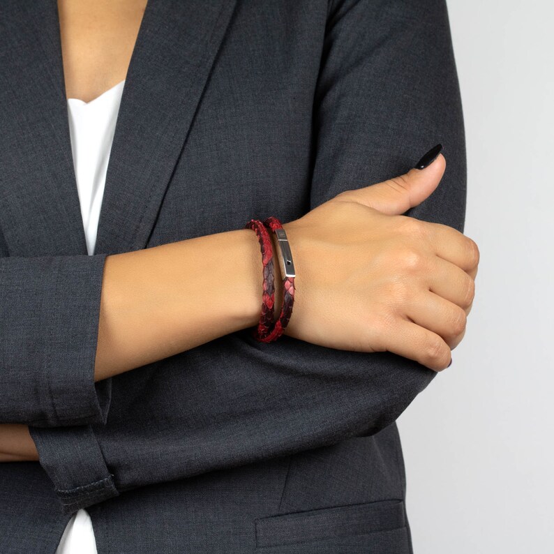 Puede incluir: Un brazalete de cuero rojo y negro con un cierre plateado. El brazalete se lleva en la mu&ntilde;eca.
