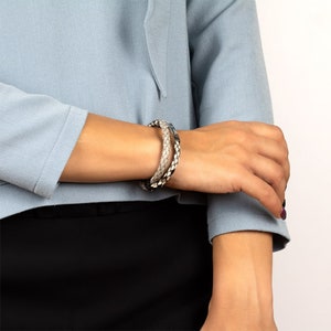 May include: A braided leather bracelet with a silver clasp. The bracelet is made of two strands of leather, one black and one white.