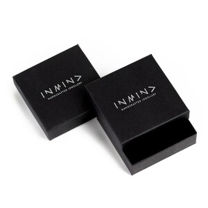 Puede incluir: Dos cajas cuadradas negras con el logotipo "INMN> HANDCRAFTED JEWELLERY" impreso en plata en la parte superior de cada caja.