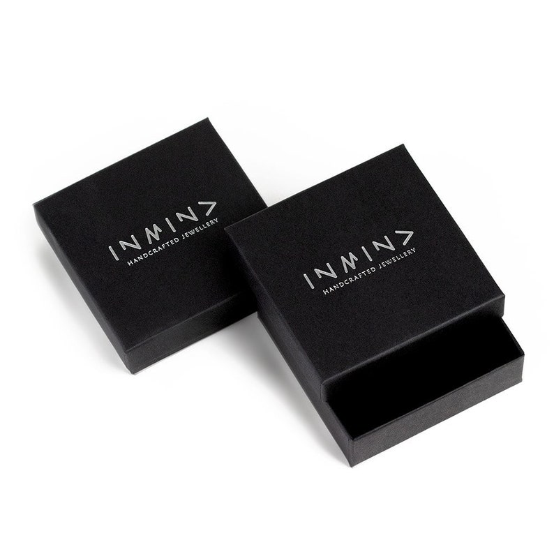 Puede incluir: Dos cajas cuadradas negras con el logotipo "INMN> HANDCRAFTED JEWELLERY" impreso en plata en la parte superior de cada caja.