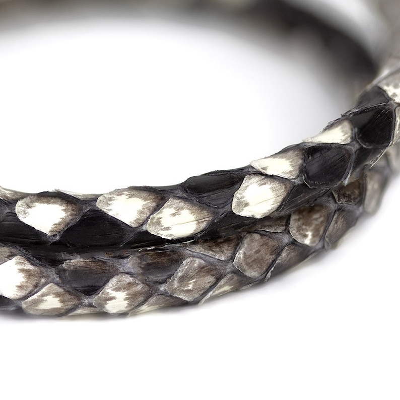 May include: Close-up of a black and white snakeskin leather cord. The cord is coiled and the texture of the skin is visible.