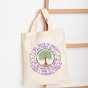 Könnte beinhalten: Eine Tragetasche aus natürlichem Canvas mit einem kreisförmigen Design, das einen Baum mit grünen Blättern und dem Text "I see trees of green, red roses too... What a wonderful world" zeigt. Das Design ist lila und schwarz.