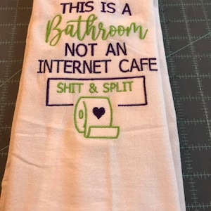 K&ouml;nnte beinhalten: Wei&szlig;es Badehandtuch mit gesticktem Text in Gr&uuml;n und Lila. Der Text lautet "THIS IS A BATHROOM NOT AN INTERNET CAFE SHIT & SPLIT" mit einer Toilettenpapierrollen-Grafik.