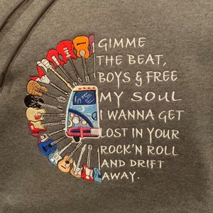 Puede incluir: Una sudadera gris con un diseño bordado de una furgoneta vintage rodeada de guitarras y el texto "GIMME THE BEAT, BOYS & FREE MY SOUL I WANNA GET LOST IN YOUR ROCK'N ROLL AND DRIFT AWAY."