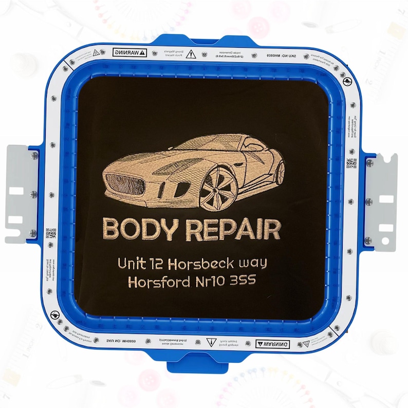 Monochrome embroidery of a sports car and business text “Body Repair, Unit 12 Horsbeck Way, Horsford Nr10 3SS,” stitched in light brown thread on black fabric inside a hoop.