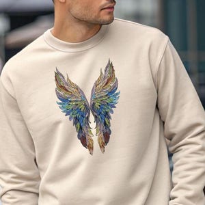 May include: A beige sweatshirt featuring a colorful, detailed illustration of angel wings. The wings are depicted with a variety of colors, including blue, green, yellow, and brown, creating a vibrant and artistic design. The sweatshirt has a crew neck.