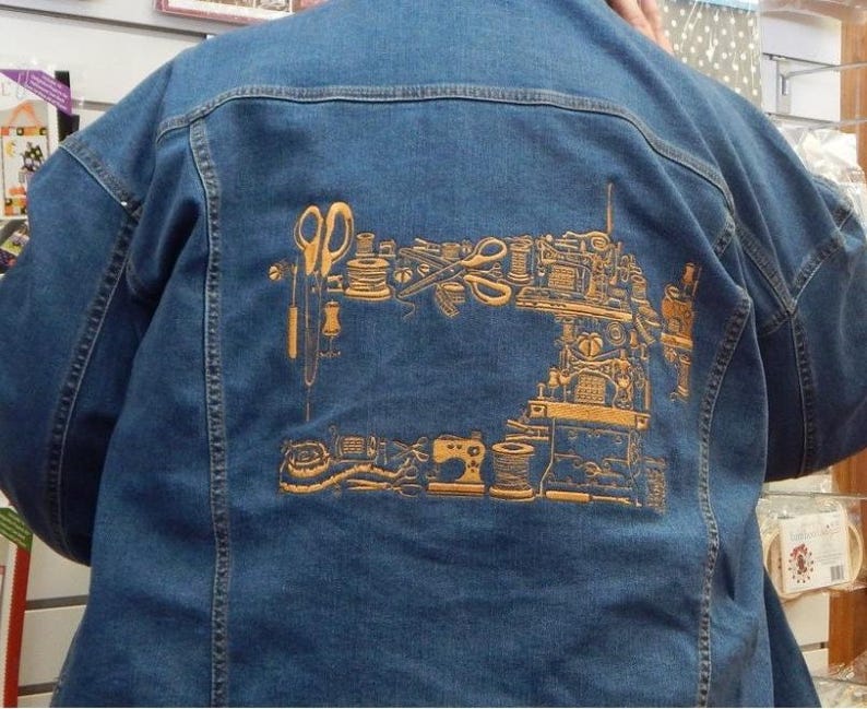 Puede incluir: Chaqueta vaquera azul con un dise&ntilde;o dorado de una m&aacute;quina de coser y herramientas de costura en la espalda. El dise&ntilde;o incluye tijeras, carretes de hilo y una m&aacute;quina de coser. La chaqueta tiene un estilo cl&aacute;sico vaquero.