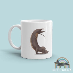 May include: White ceramic mug featuring a whimsical illustration of a brown dachshund in a yoga pose. The dog is arched, with its tail and legs extended. The mug has a handle on the left side. The bottom right corner has a logo with a dog and the text "MEET WILMA".