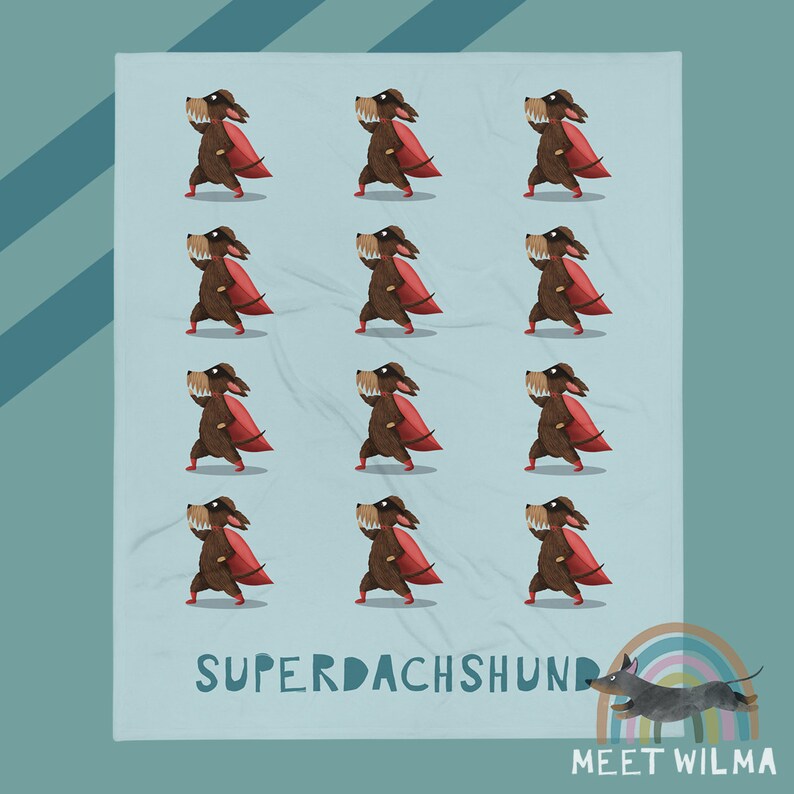 May include: A light blue blanket with a repeating pattern of cartoon dachshunds in superhero costumes with red capes. The words "SUPERDACHSHUND" are printed in white. A small illustration of a dachshund and rainbow is in the corner.