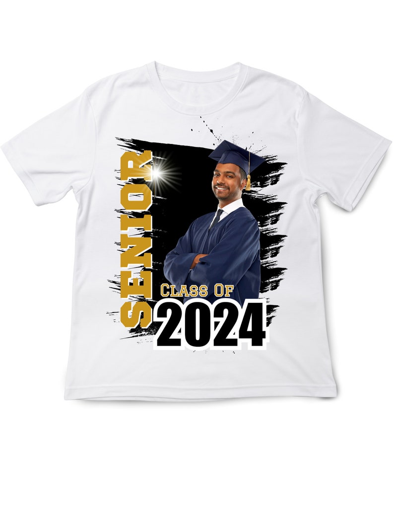 May include: White t-shirt featuring a graduation theme. The shirt has the word "SENIOR" in gold, the text "CLASS OF 2024" in black, and a photo of a graduate in a cap and gown. The background has black brush strokes.