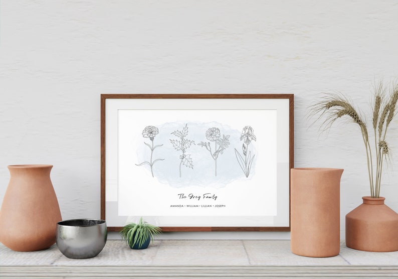 Puede incluir: Una impresi&oacute;n enmarcada con un marco de madera marr&oacute;n que presenta cuatro flores dibujadas a l&iacute;nea sobre un fondo de acuarela azul. El texto "The Grey Family" y los nombres est&aacute;n debajo. Jarrones decorativos y una peque&ntilde;a planta en el estante.
