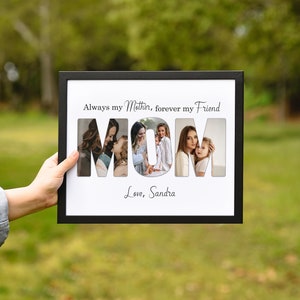 May include: A black framed photo collage with the word "MOM" cut out to reveal four family photos. The text above reads "Always my Mother, forever my Friend" and below "Love, Sandra". The frame is held against a blurred green background.