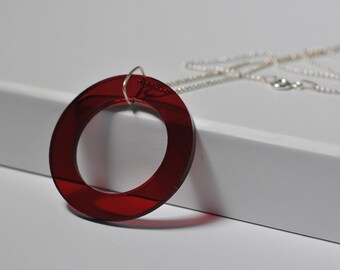 Puede incluir: Un collar con un colgante circular de acrílico rojo y una cadena plateada.