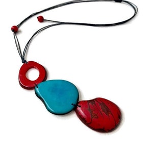 May include: A necklace with a black cord and three red and turquoise ceramic beads. The beads are shaped like ovals and circles.