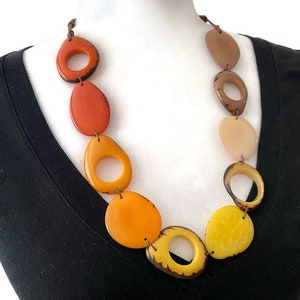 Könnte beinhalten: Eine lange Halskette mit großen, bunten, ovalen Perlen. Die Perlen sind in Orange-, Gelb- und Brauntönen gehalten. Die Halskette besteht aus einer braunen Schnur.