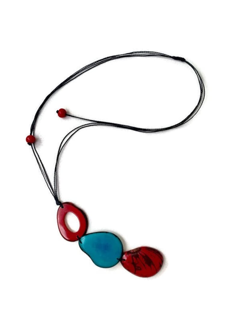 May include: A necklace with a black cord and three pendant charms. The charms are shaped like an oval, a teardrop, and a rounded rectangle. The oval and rectangle charms are red, and the teardrop charm is blue.