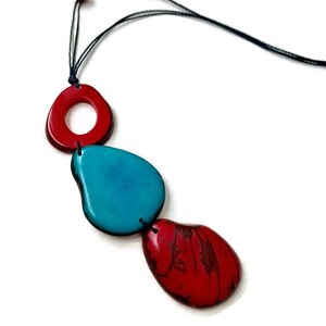 May include: A necklace with three colorful, organic-shaped beads. The beads are red, turquoise, and red. The necklace is made of black cord.