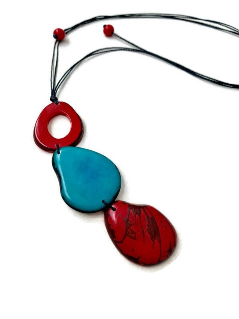 May include: A necklace with three colorful, organic-shaped beads. The beads are red, turquoise, and red. The necklace is made of black cord.