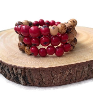 May include: Three stacked bracelets made of red and natural wood beads. The bracelets are on a wooden surface.