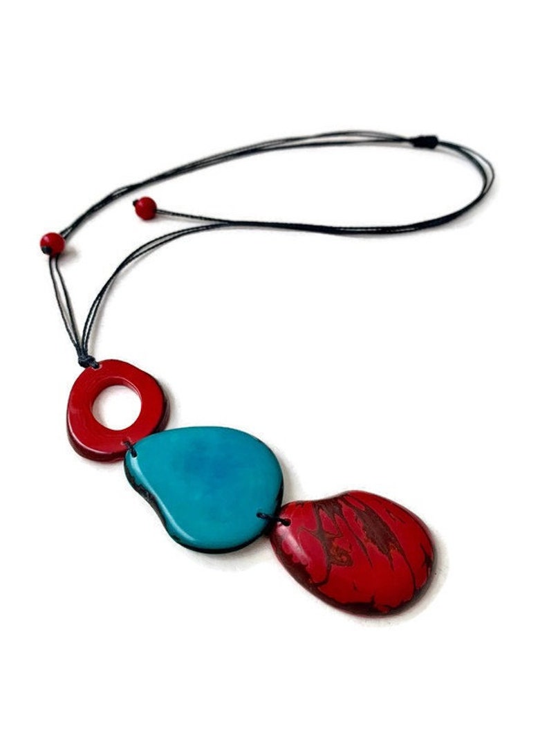 May include: A necklace with a black cord and three red and turquoise ceramic beads. The beads are shaped like ovals and circles.