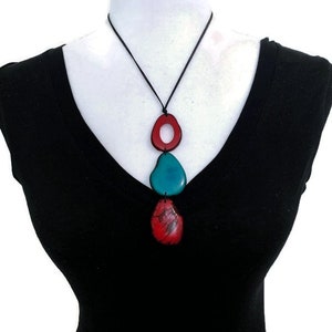 May include: A necklace with three wooden beads. The top bead is red and has a hole in the center. The middle bead is teal blue and the bottom bead is red. The necklace is on a black cord.