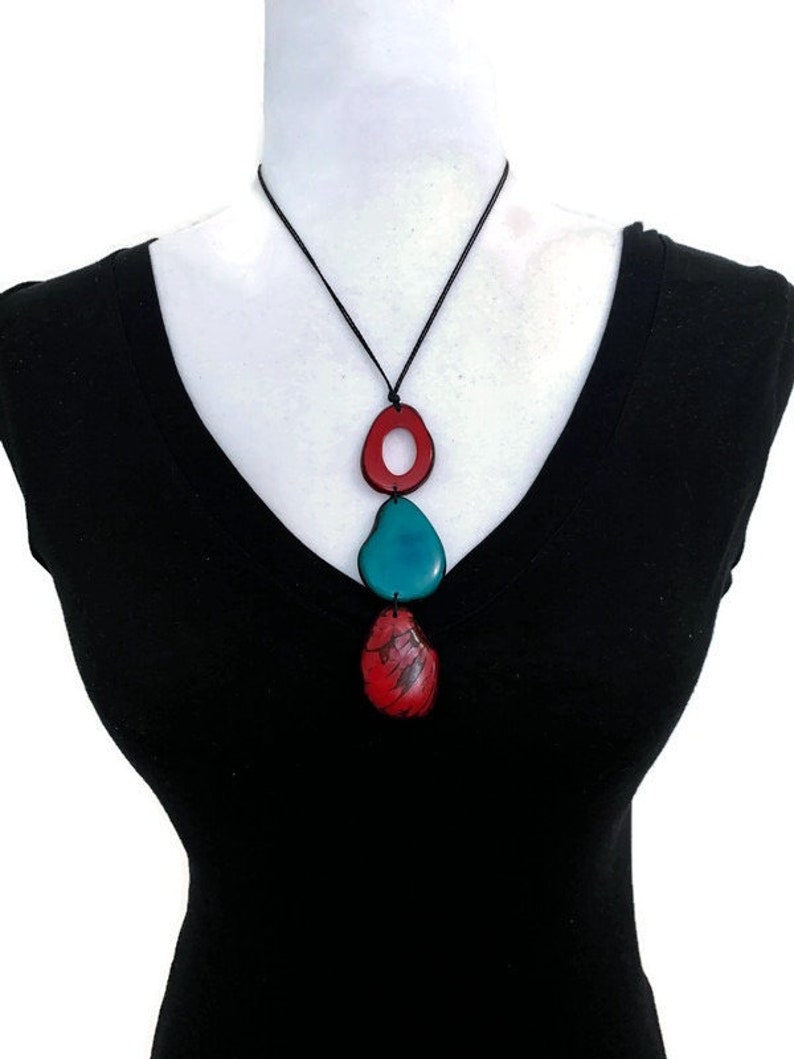 May include: A necklace with three wooden beads. The top bead is red and has a hole in the center. The middle bead is teal blue and the bottom bead is red. The necklace is on a black cord.