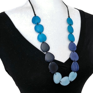 May include: A long necklace made of large, round, graduated blue and teal coloured beads. The beads are strung on a black cord.