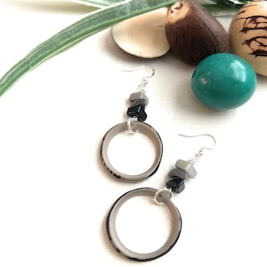 May include: A pair of silver hoop earrings with grey and black beads hanging from them. The hoops are made of a natural material, possibly wood or bone.