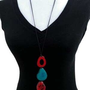 May include: A long necklace with a black cord and three pendant charms. The charms are in the shape of ovals and are red, blue, and green.