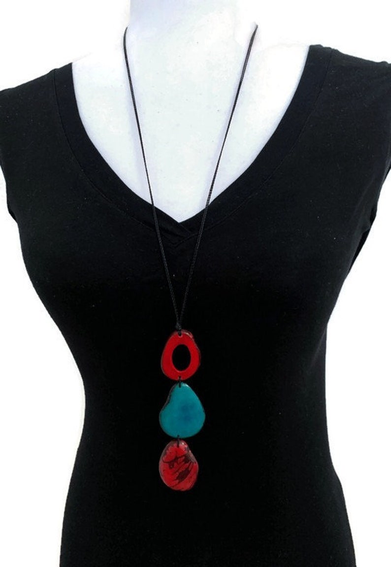 May include: A long necklace with a black cord and three pendant charms. The charms are in the shape of ovals and are red, blue, and green.